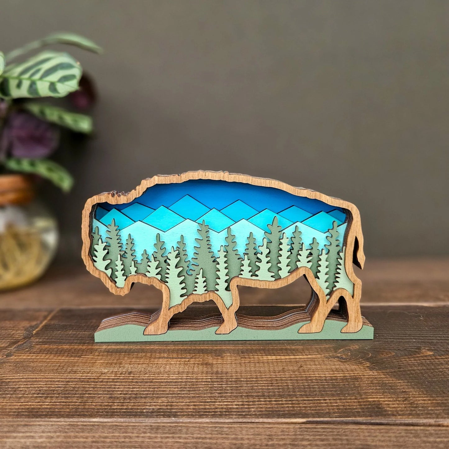 Wooden buffalo sculpture with a mountain and forest design on a wooden surface