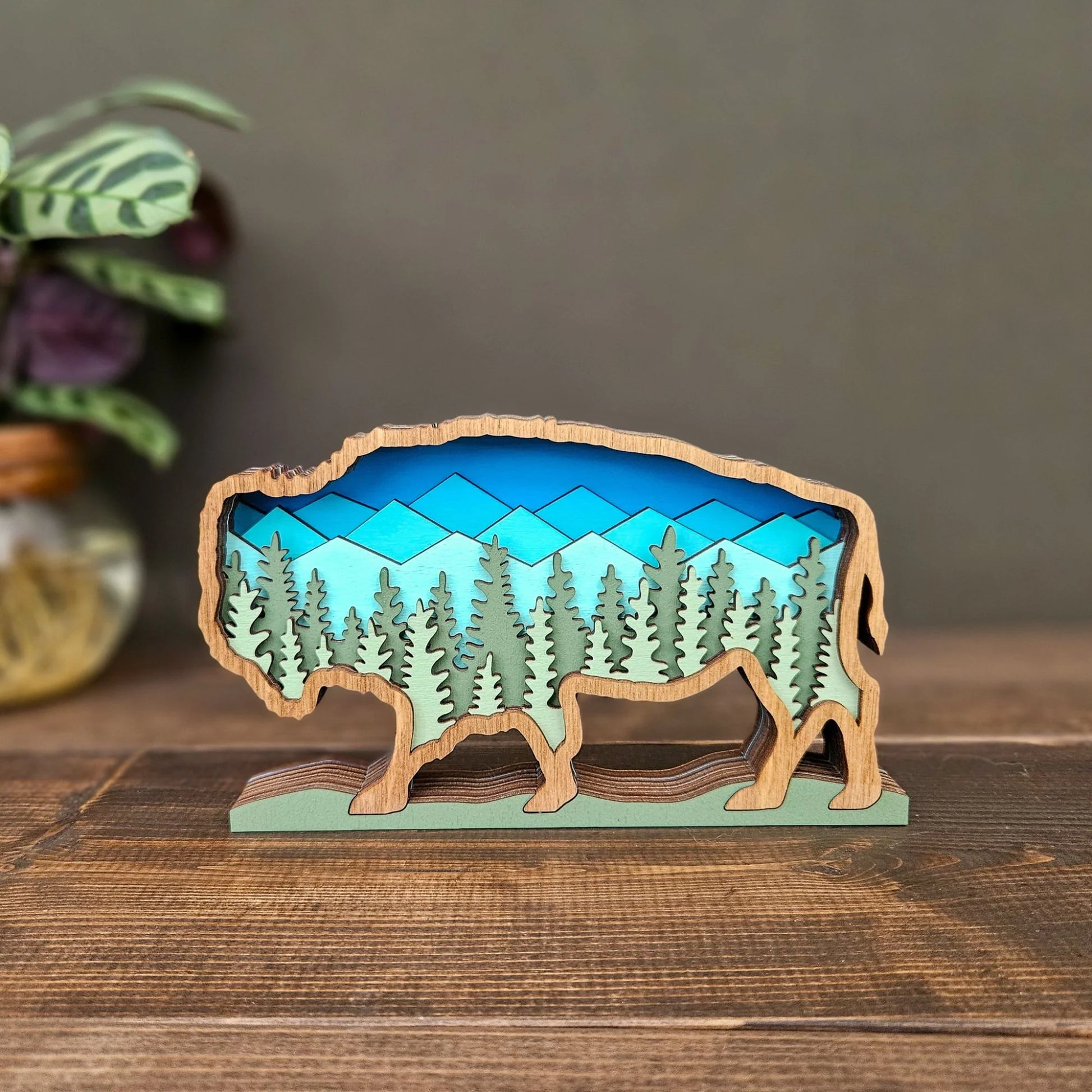 Wooden buffalo sculpture with a mountain and forest design on a wooden surface